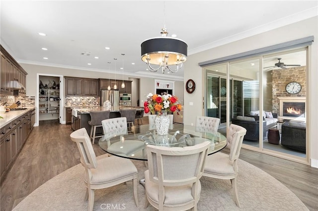 dining room with light hardwood / wood-style flooring, crown molding, and a stone fireplace