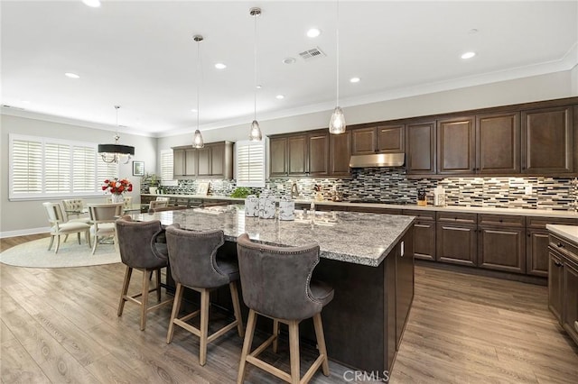 kitchen featuring a kitchen bar, hanging light fixtures, hardwood / wood-style flooring, and a center island with sink