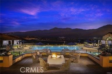 pool at dusk featuring an outdoor fire pit, a patio area, and a mountain view