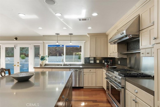 kitchen with tasteful backsplash, decorative light fixtures, stainless steel appliances, cream cabinets, and wall chimney range hood