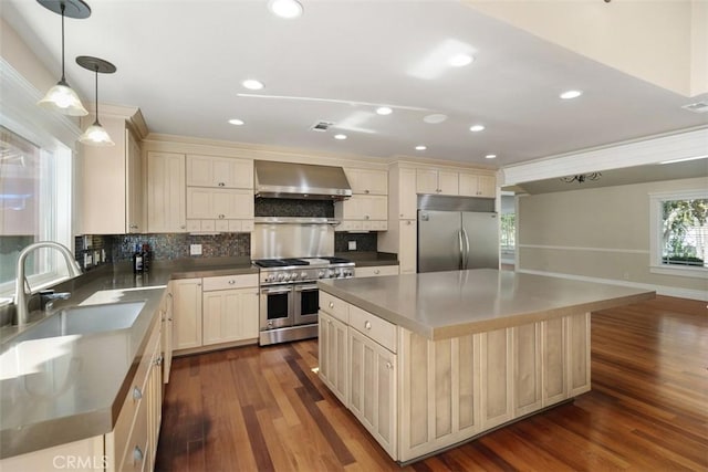 kitchen with dark wood-type flooring, wall chimney exhaust hood, sink, high quality appliances, and a kitchen island