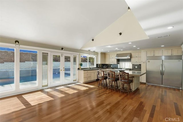 kitchen with built in fridge, a kitchen island, pendant lighting, a kitchen bar, and wall chimney exhaust hood