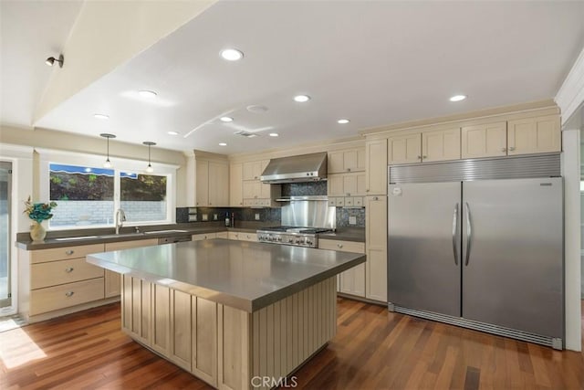 kitchen with stove, hanging light fixtures, a center island, built in fridge, and wall chimney exhaust hood