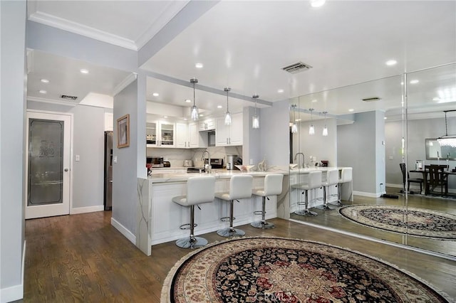 kitchen with pendant lighting, dark wood-type flooring, white cabinetry, sink, and a breakfast bar area