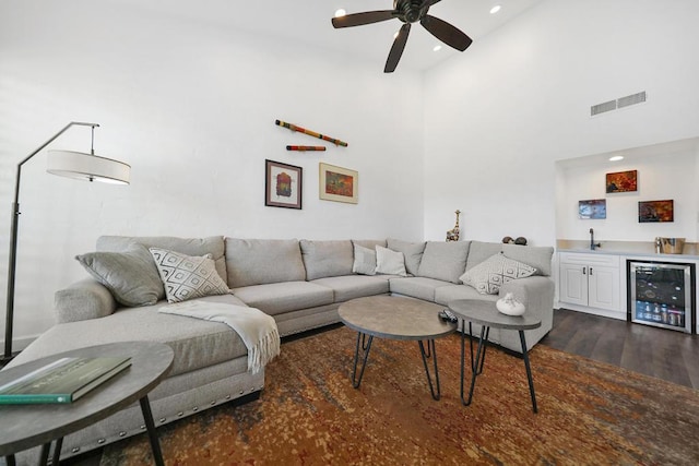 living room featuring wine cooler, ceiling fan, dark wood-type flooring, a towering ceiling, and indoor wet bar