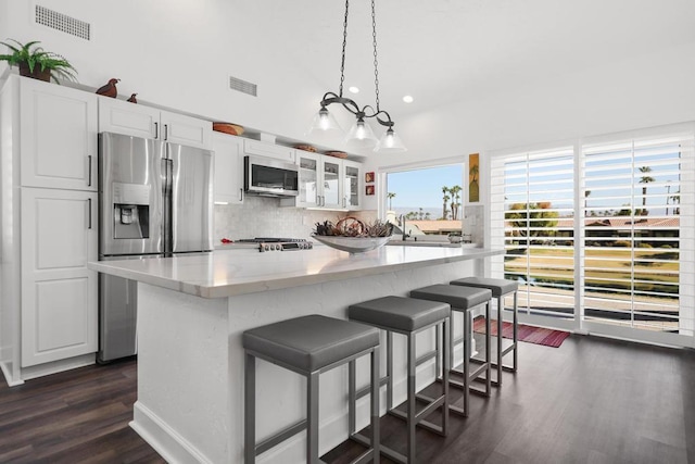 kitchen with appliances with stainless steel finishes, decorative light fixtures, tasteful backsplash, white cabinetry, and a center island