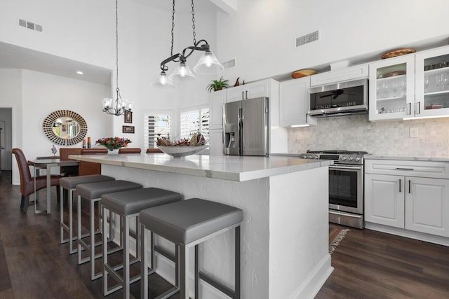 kitchen featuring a towering ceiling, white cabinetry, stainless steel appliances, tasteful backsplash, and hanging light fixtures