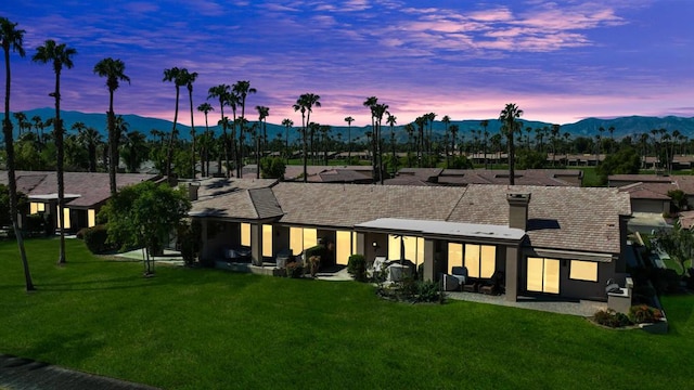 back house at dusk with a mountain view and a yard