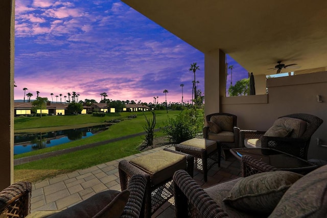 patio terrace at dusk featuring ceiling fan and a water view