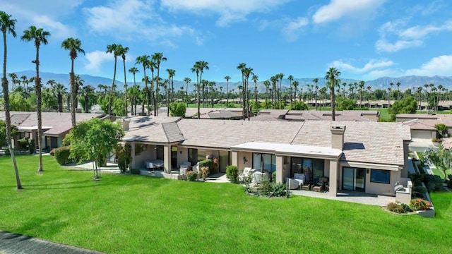 rear view of property featuring a mountain view, a patio area, and a lawn