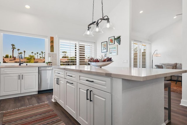 kitchen featuring stainless steel dishwasher, vaulted ceiling, hanging light fixtures, white cabinetry, and a breakfast bar