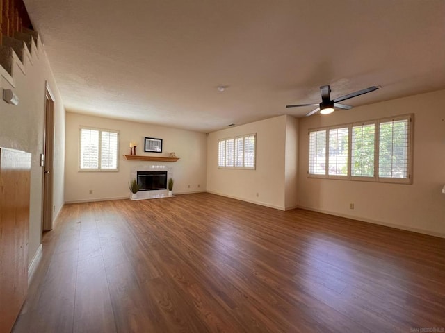 unfurnished living room featuring ceiling fan, wood-type flooring, and a tiled fireplace