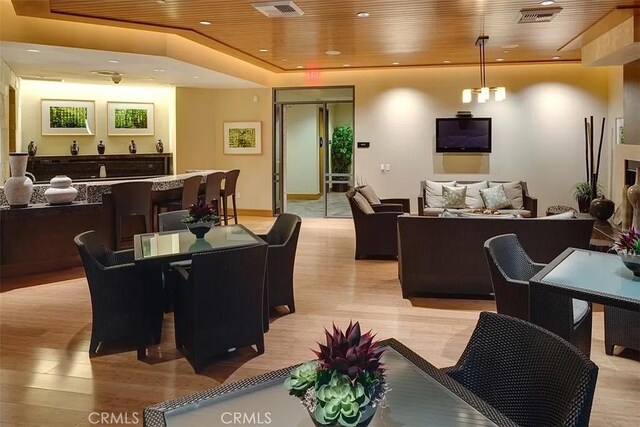 dining space with light wood-type flooring, wood ceiling, and a tray ceiling