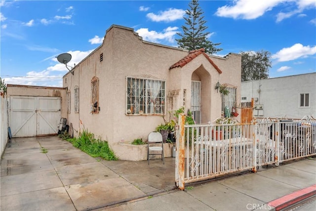 mediterranean / spanish-style house with a tile roof, a gate, fence, and stucco siding