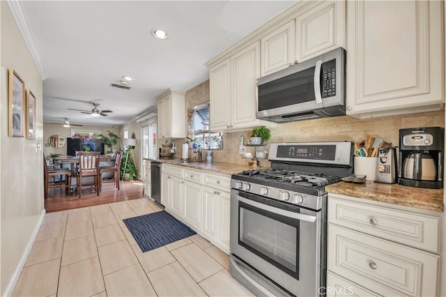 kitchen with light tile patterned flooring, ceiling fan, appliances with stainless steel finishes, and light stone countertops