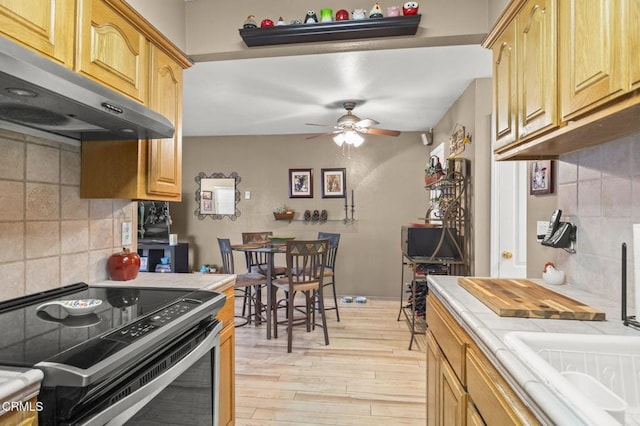 kitchen with electric stove, exhaust hood, backsplash, tile countertops, and light wood-type flooring