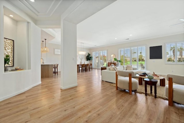 living room featuring light wood-type flooring, ceiling fan with notable chandelier, and crown molding