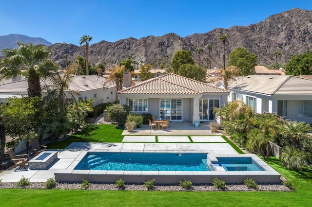 back of property with a mountain view, a patio area, a yard, and a fire pit