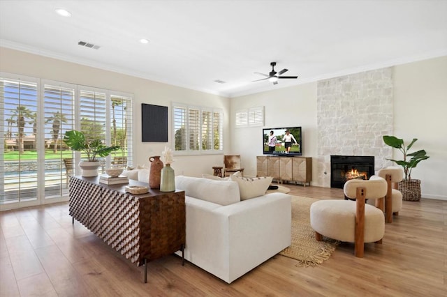 living room featuring ceiling fan, ornamental molding, light hardwood / wood-style floors, and a fireplace