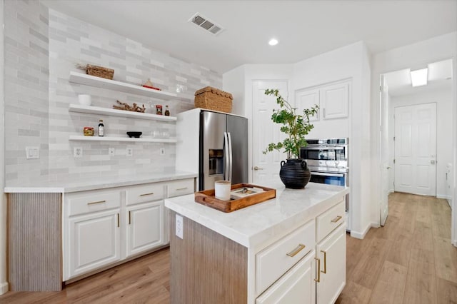 kitchen featuring white cabinets, appliances with stainless steel finishes, a kitchen island, decorative backsplash, and light hardwood / wood-style floors