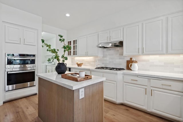 kitchen featuring white cabinetry, appliances with stainless steel finishes, backsplash, light wood-type flooring, and a center island