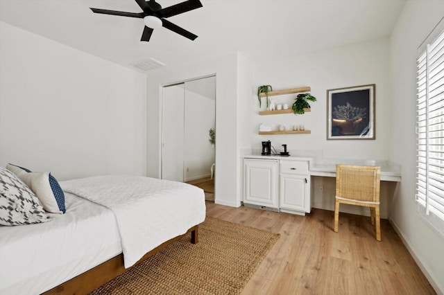 bedroom featuring ceiling fan, a closet, built in desk, and light wood-type flooring