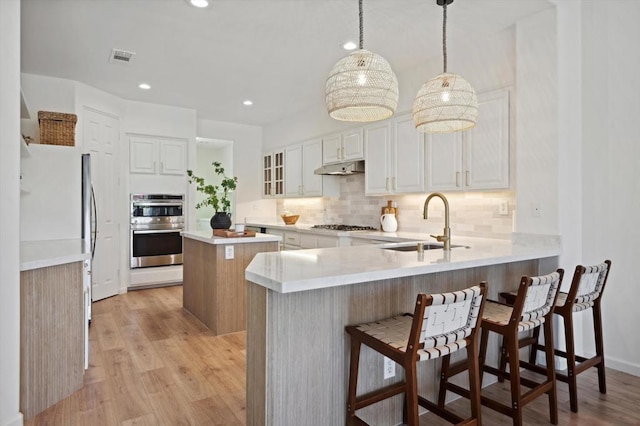 kitchen with kitchen peninsula, sink, hanging light fixtures, stainless steel appliances, and white cabinets