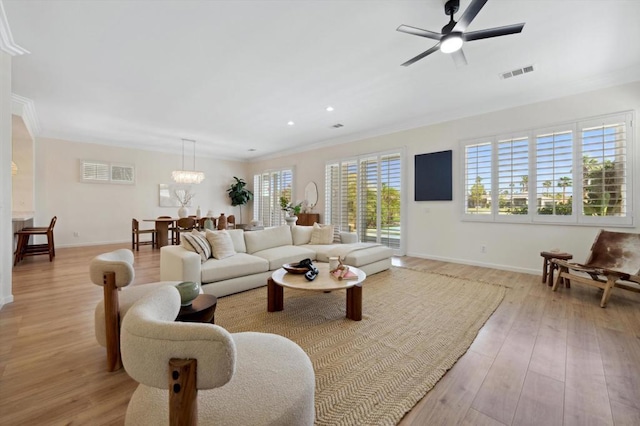 living room with light wood-type flooring, ceiling fan with notable chandelier, and ornamental molding