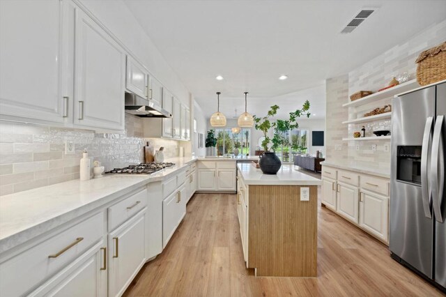 kitchen with white cabinets, a kitchen island, decorative light fixtures, stainless steel appliances, and tasteful backsplash