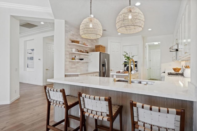 kitchen featuring kitchen peninsula, a kitchen bar, sink, stainless steel fridge with ice dispenser, and white cabinets