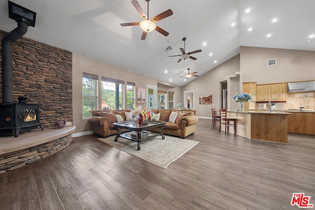 living room featuring high vaulted ceiling, ceiling fan, a wood stove, and hardwood / wood-style floors