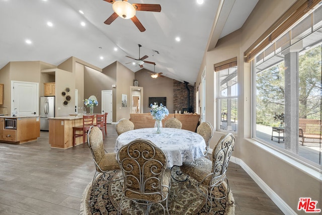 dining space featuring plenty of natural light, wood-type flooring, a wood stove, and vaulted ceiling