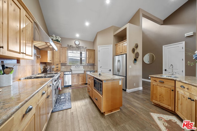 kitchen with a kitchen island, sink, light wood-type flooring, light stone countertops, and appliances with stainless steel finishes