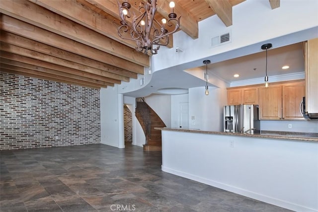 kitchen featuring pendant lighting, brick wall, beamed ceiling, dark stone countertops, and stainless steel fridge