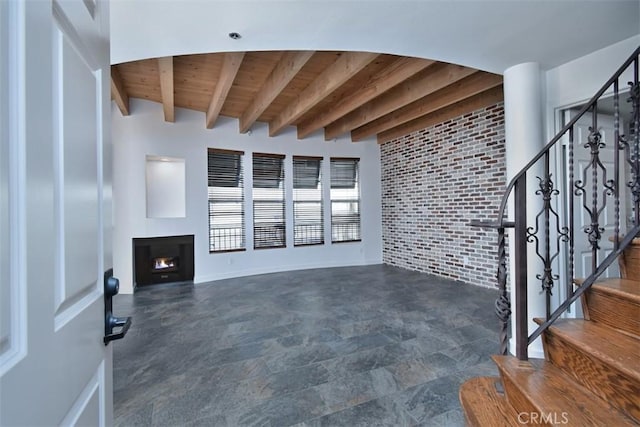 unfurnished living room featuring wooden ceiling, brick wall, and beamed ceiling