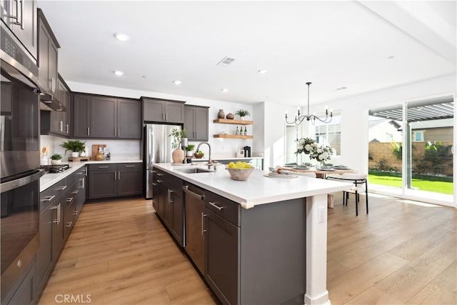 kitchen with a chandelier, a kitchen island with sink, light hardwood / wood-style floors, and sink