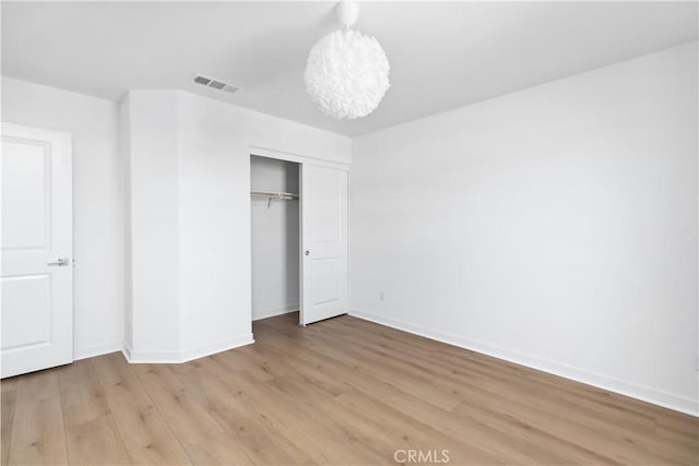 unfurnished bedroom featuring a closet, hardwood / wood-style flooring, and an inviting chandelier