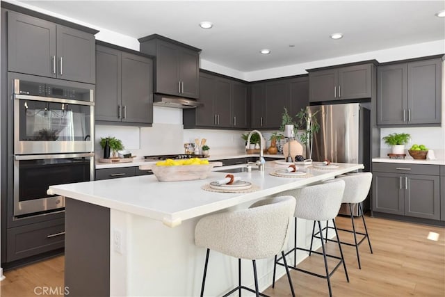 kitchen featuring appliances with stainless steel finishes, light hardwood / wood-style floors, sink, a kitchen breakfast bar, and a kitchen island with sink