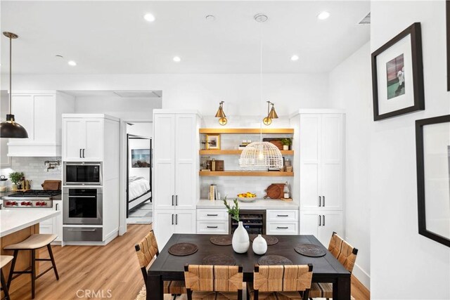 kitchen featuring pendant lighting, white cabinetry, stainless steel appliances, backsplash, and light wood-type flooring