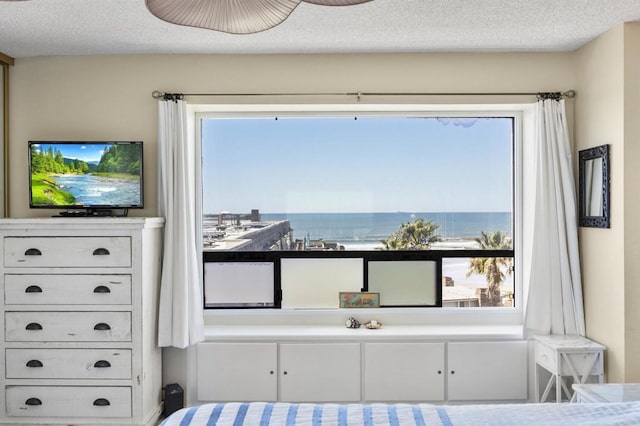 bedroom featuring a water view, a textured ceiling, and multiple windows