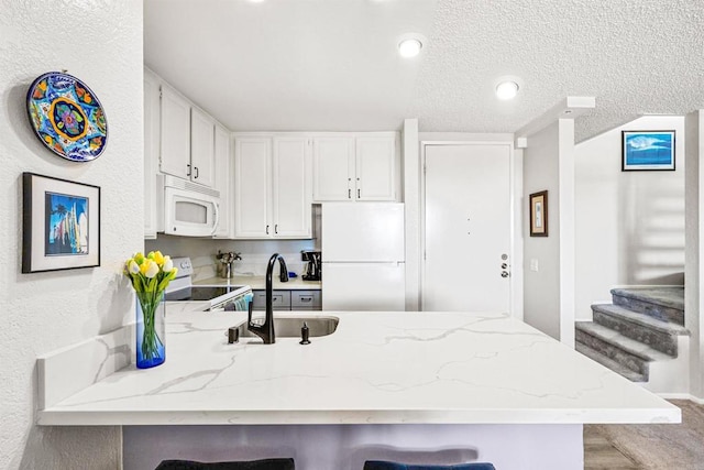 kitchen featuring white appliances, white cabinetry, sink, kitchen peninsula, and a breakfast bar