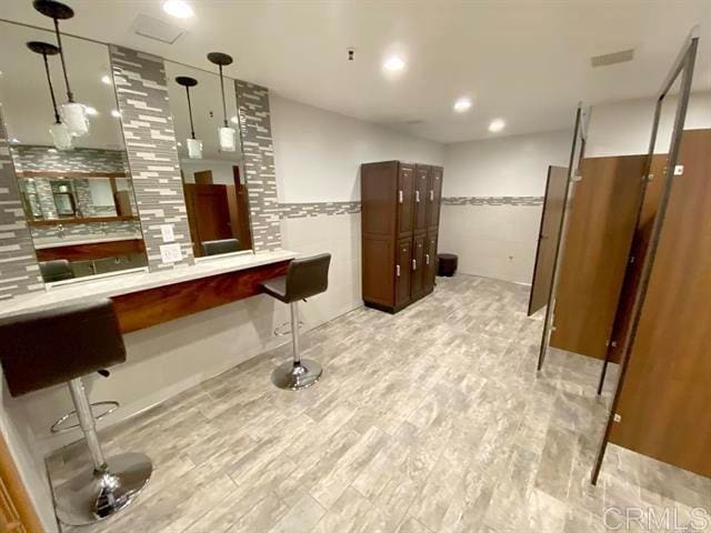 bar with light wood-type flooring, tile walls, backsplash, and decorative light fixtures