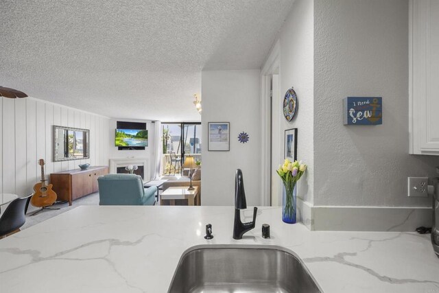 kitchen featuring light stone countertops, a textured ceiling, white cabinetry, sink, and wood walls