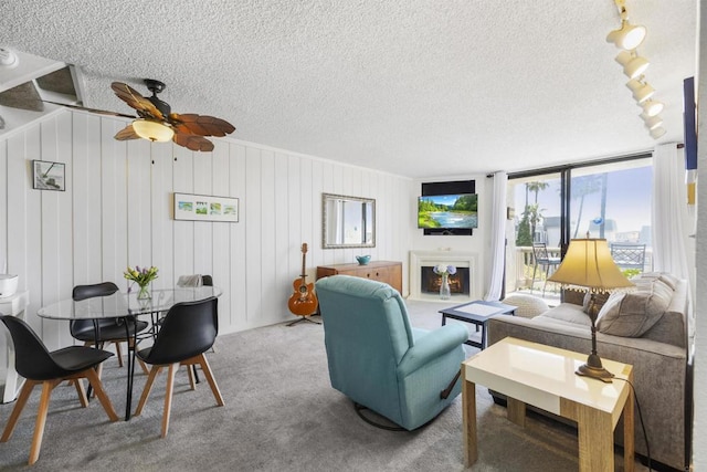 living room featuring ceiling fan, wood walls, carpet floors, and a textured ceiling