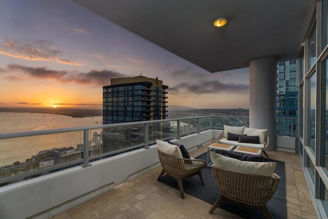 balcony at dusk featuring a water view and an outdoor living space