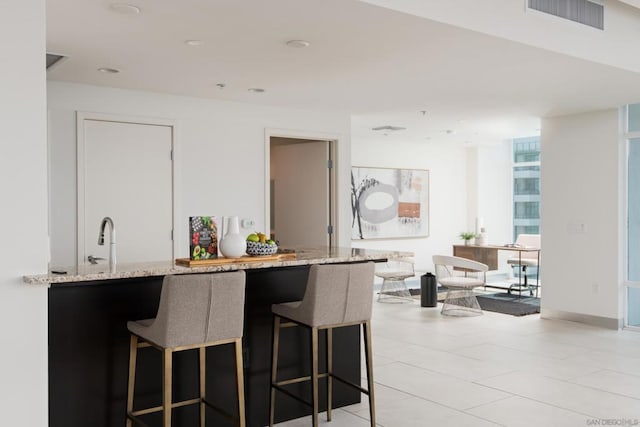 kitchen with light stone counters, sink, a wall of windows, and a breakfast bar area