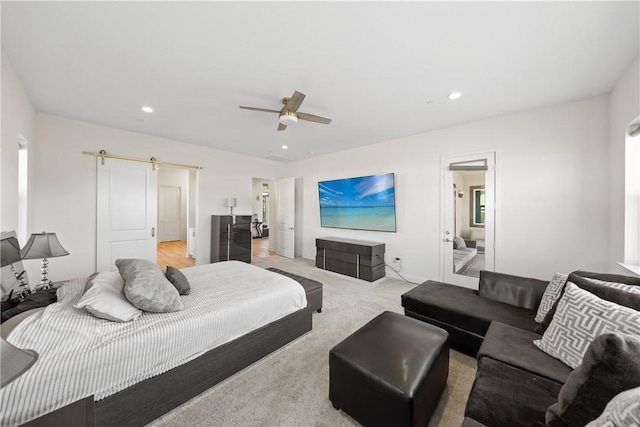 bedroom featuring ceiling fan, light colored carpet, and a barn door