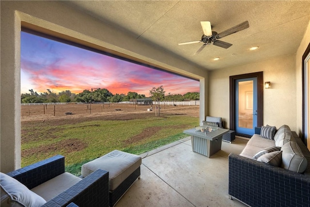 patio terrace at dusk with ceiling fan, an outdoor living space, a rural view, and a yard