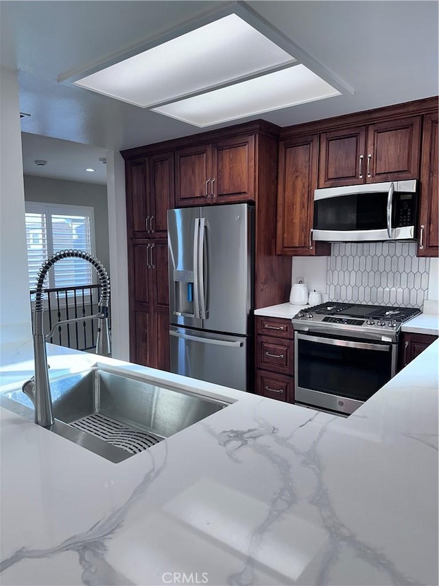 kitchen with decorative backsplash, sink, appliances with stainless steel finishes, and light stone countertops