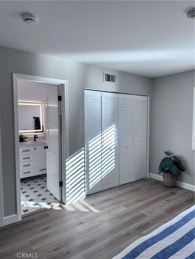 unfurnished bedroom featuring a closet, connected bathroom, light hardwood / wood-style flooring, and sink